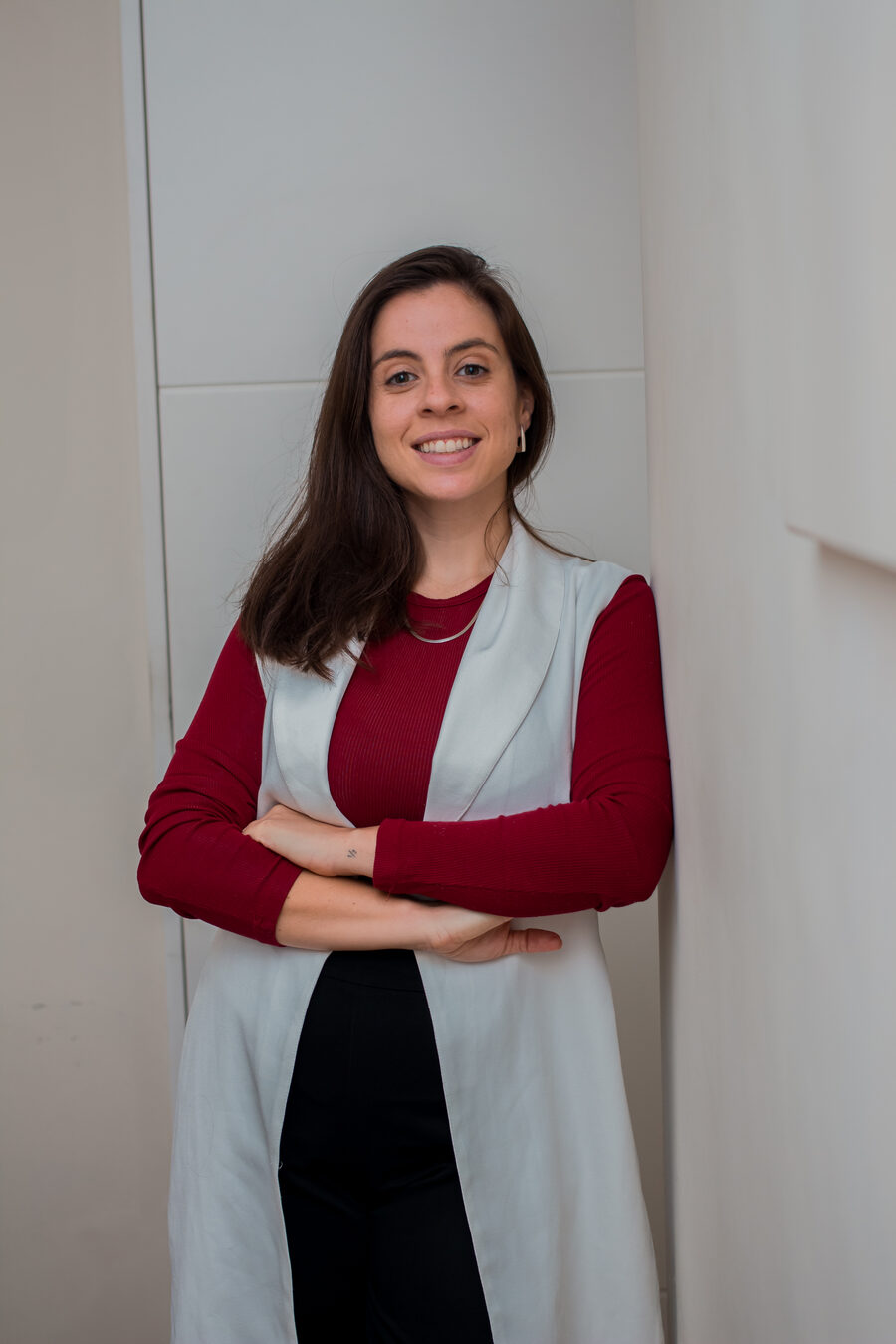 Dra. Amanda Saavedra de pé no consultório, de colete branco e braços cruzados
